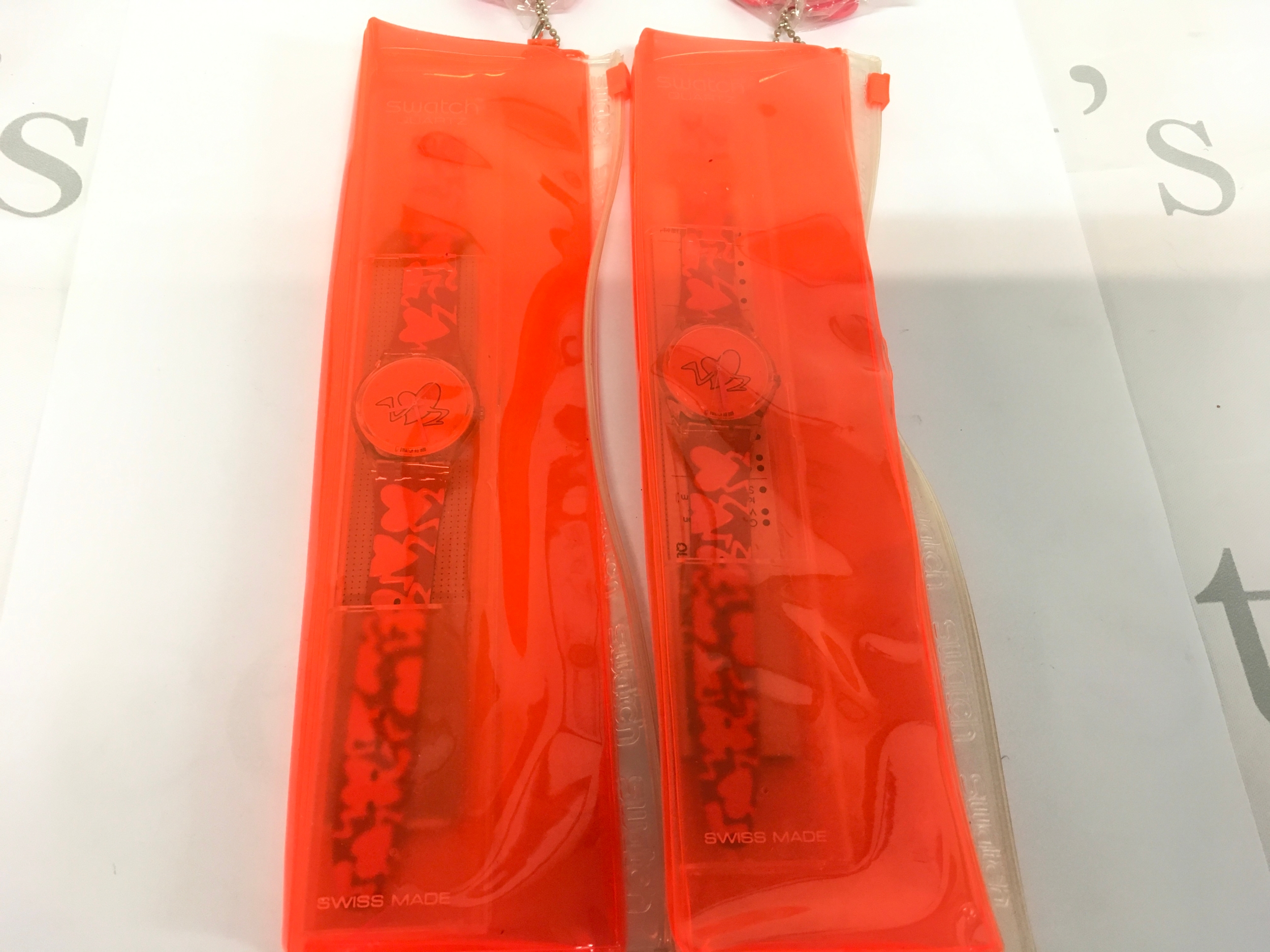 Two Vintage 1997 Swatch "Pounding Heart" watch (model GK237) released as a Valentine's Day Special. The watch features a vibrant red dial and strap decorated with stylized hearts that have feet. It comes in a special neon orange protective sleeve