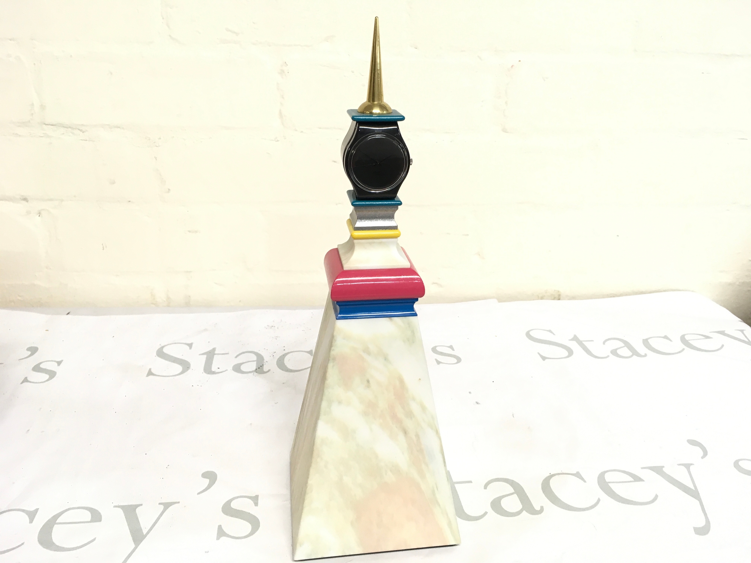 Swatch Gent Artist Special "Monumento Mendini" (Mendini Tower) designed by Alessandro Mendini in 1998. It is a limited edition piece with only 9,999 units produced, featuring quartz wristwatch atop a colorful, pyramid-shaped plastic base.