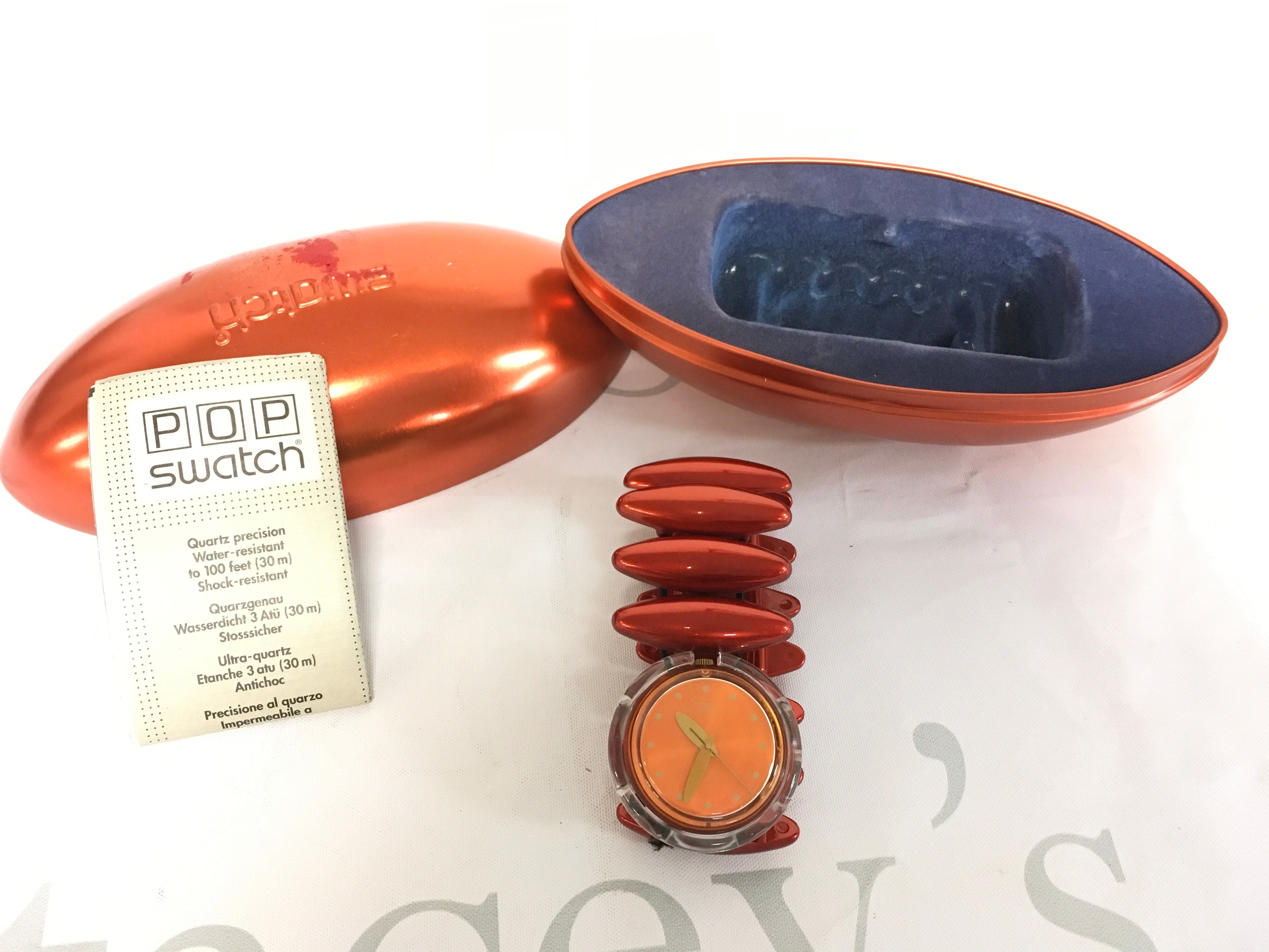 1998 Swatch Midi Pop watch in the "Neanda Orange" (PMO102) model, featuring a distinctive elastic band made of metallic orange plastic links