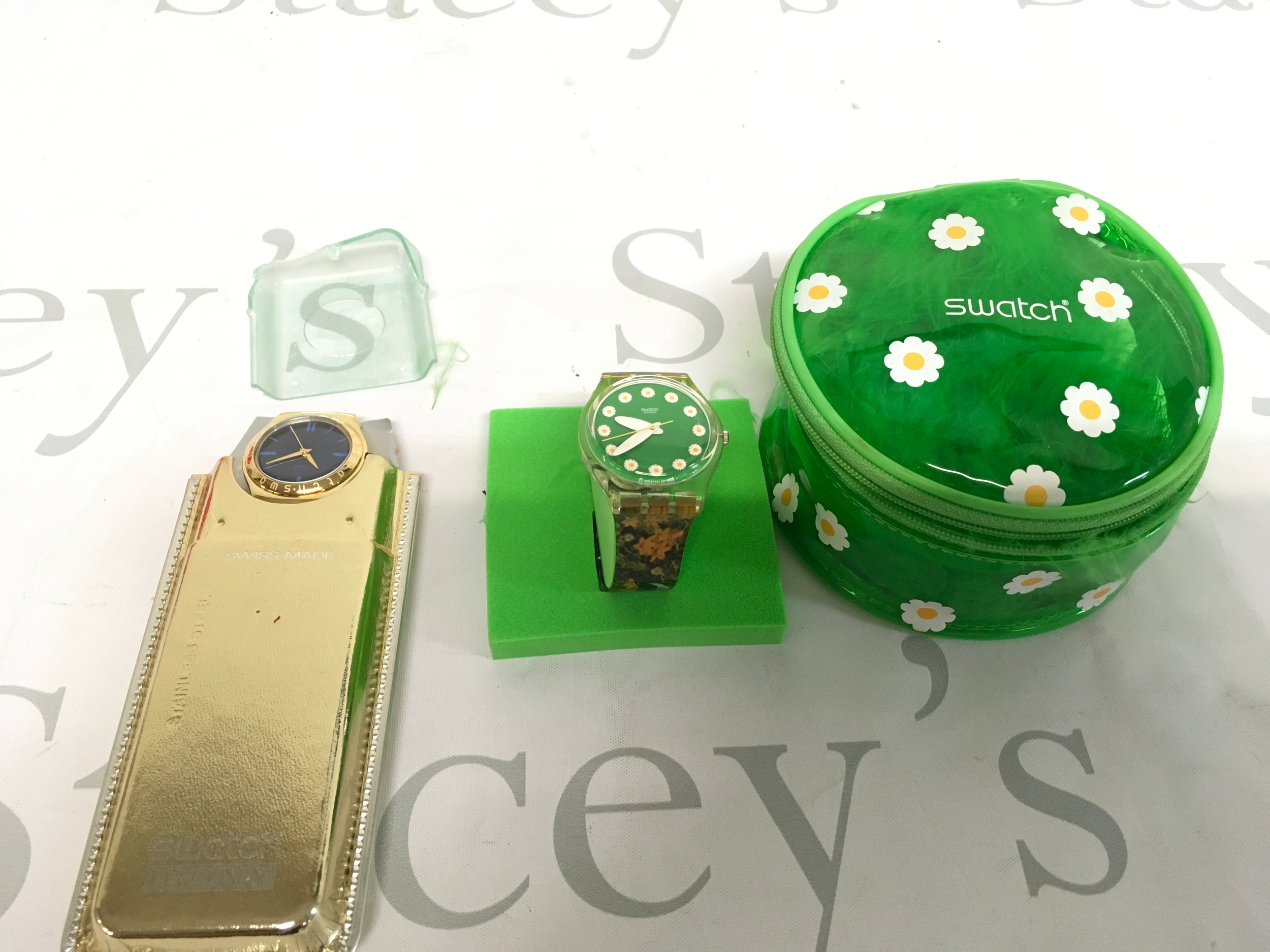 1999 Swatch Gent watch named "Where's the Egg" (GG186) with a green dial decorated with white daisies also a Swatch Irony Medium watch, specifically the "Evensong" model (YLG110) from 1997, featuring a gold-toned case and a blue dial