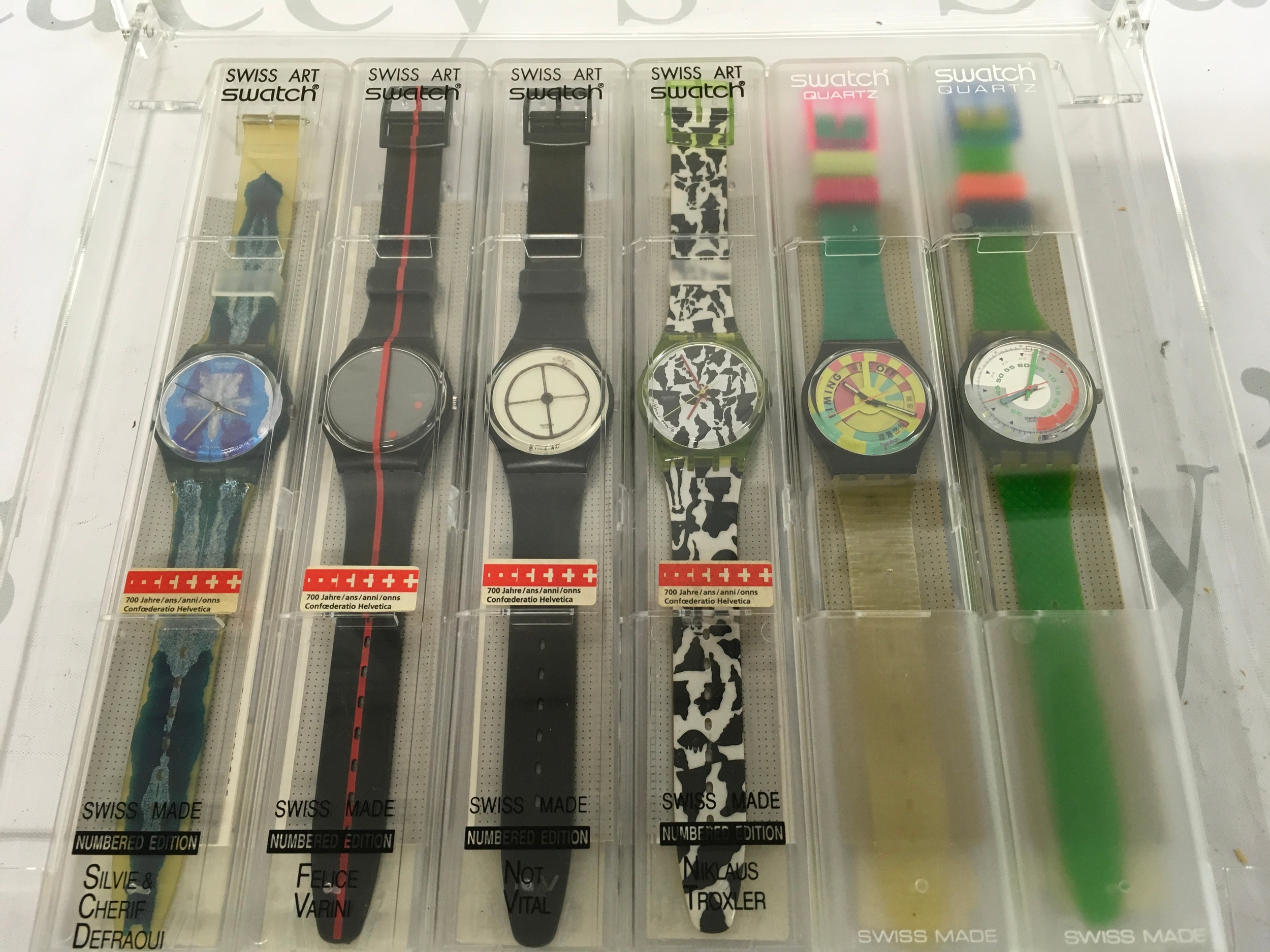 Six swatch watches including Swatch 700th Anniversary Swiss Confederation 4-piece numbered edition set from 1991, featuring limited edition watches designed by artists including Felice Varini, Not Vital, and Niklaus Troxler