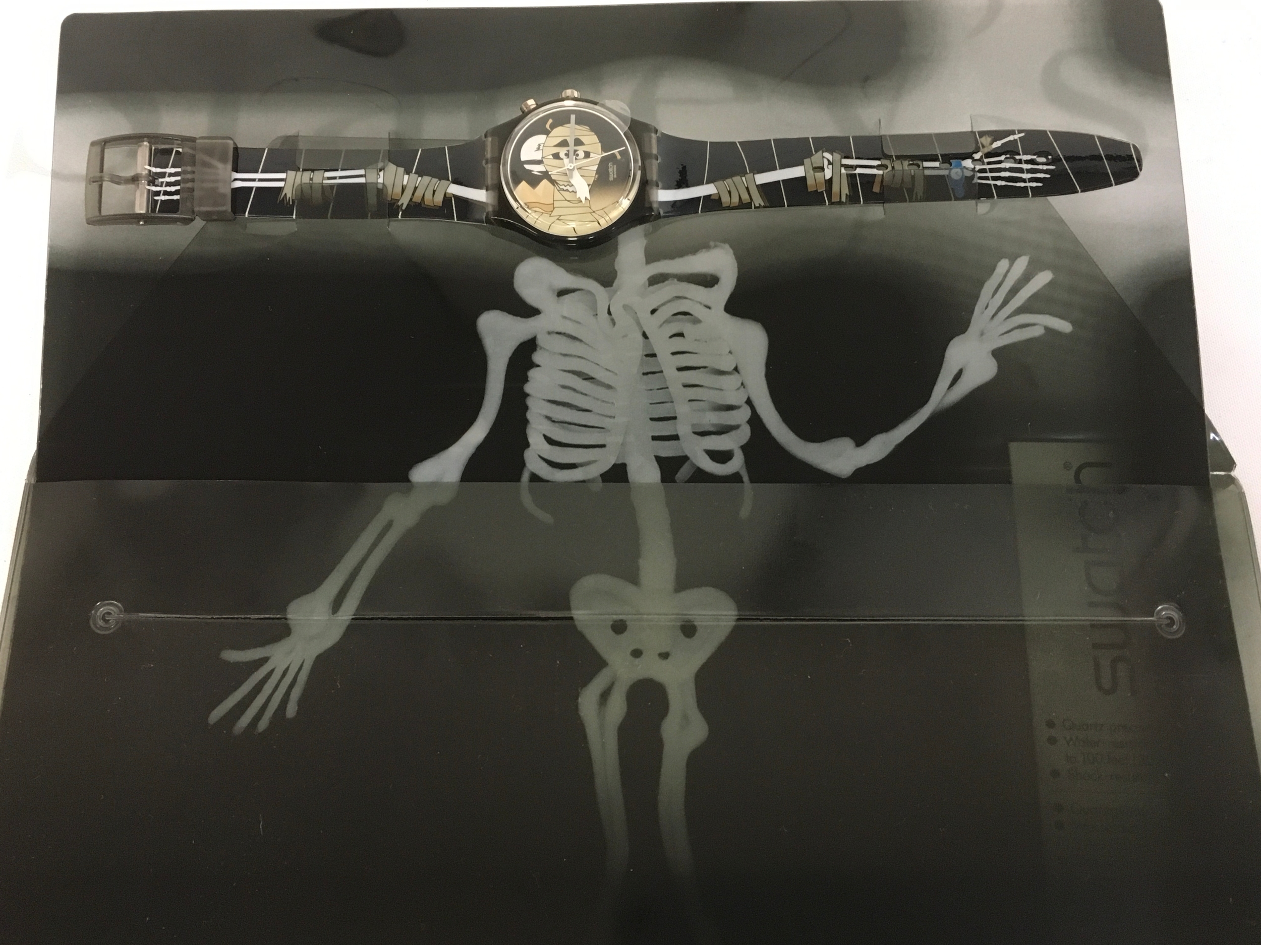 Swatch Gent Loomi MUMMIA GM900, a 2001 Halloween special edition watch featuring a unique mummy design on the dial and straps. The watch includes a Loomi backlight feature for reading the time in the dark. It comes in special X-ray style packaging designed to look like a skeleton