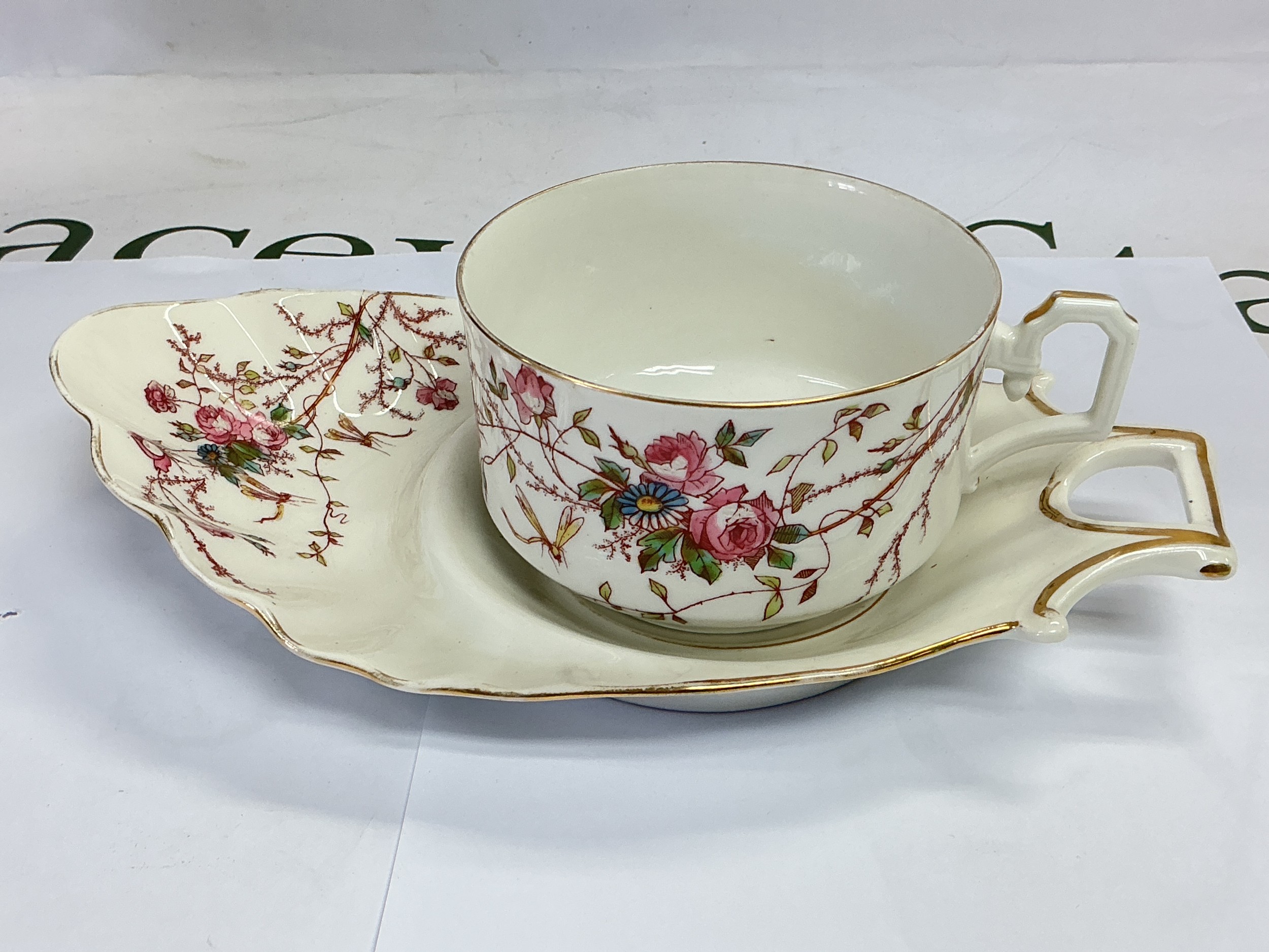 A Limoges cup and underplate with floral and insect decoration on a white ground.