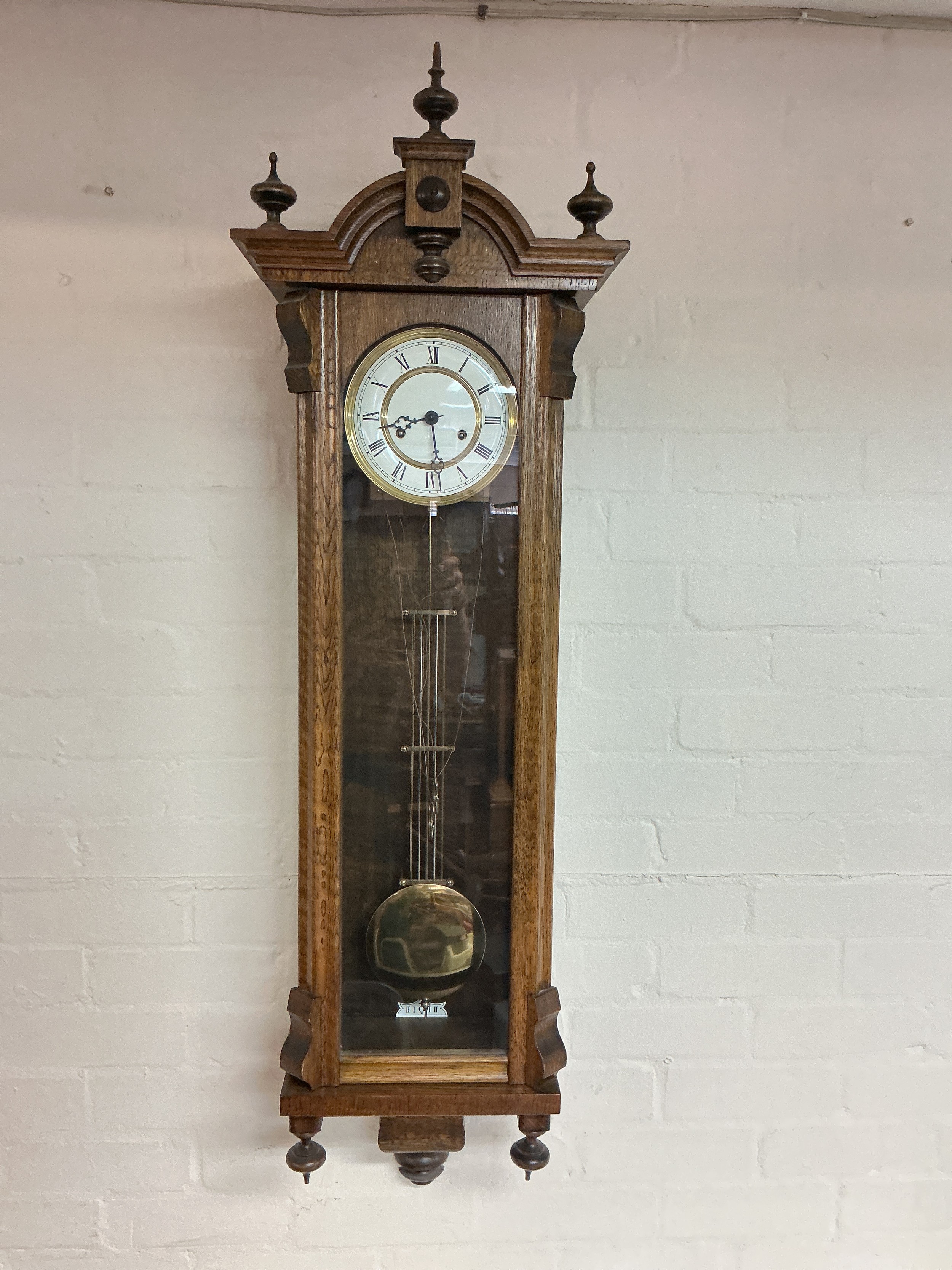 An oak wall clock with pendulum and two weights, approx height 124cm.