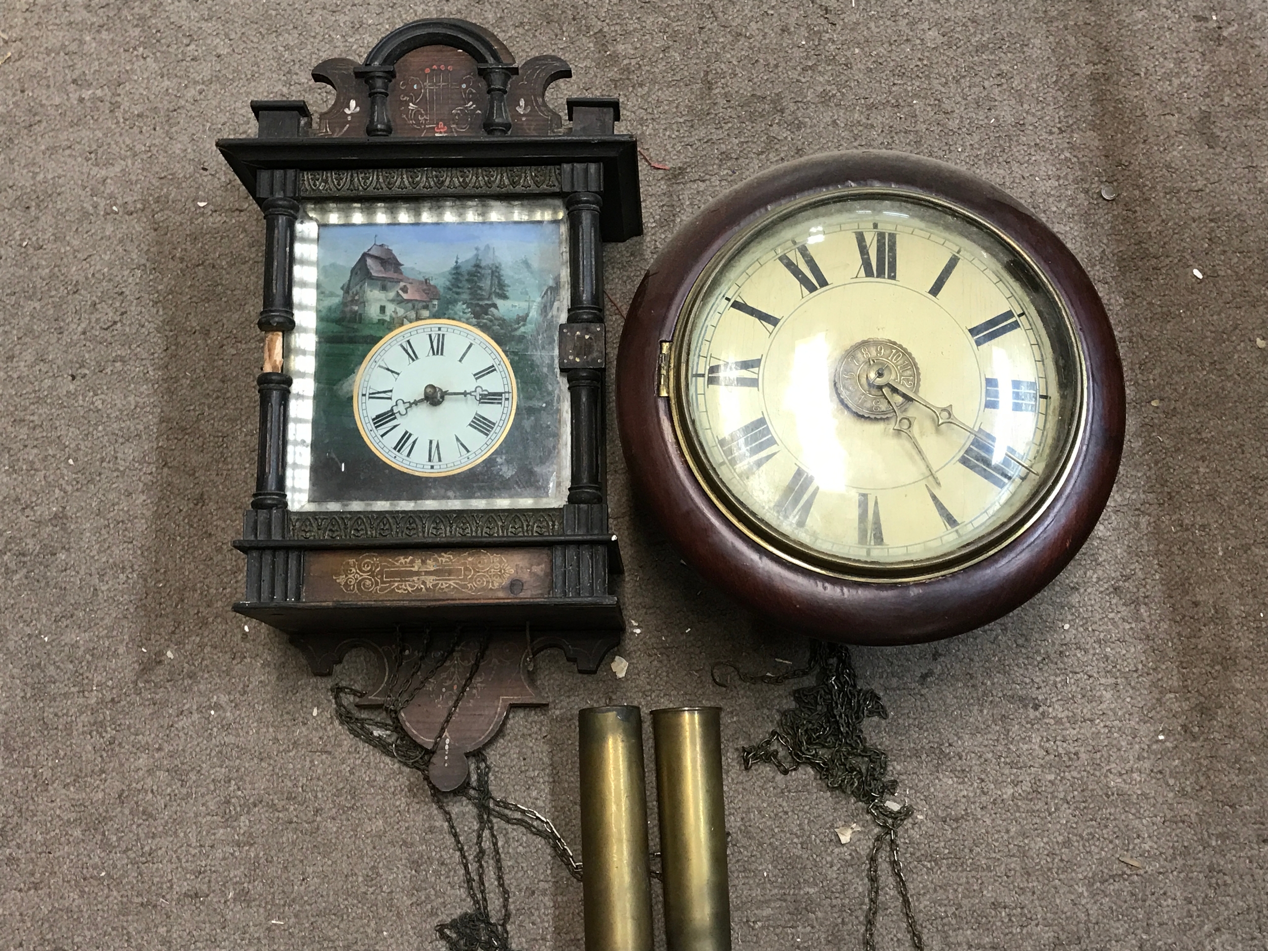 A Black Forest picture-frame wall clock featuring a painted pastoral landscape scene surrounding the clock face, accompanied by a round wooden-cased wall clock and two brass weight cylinders