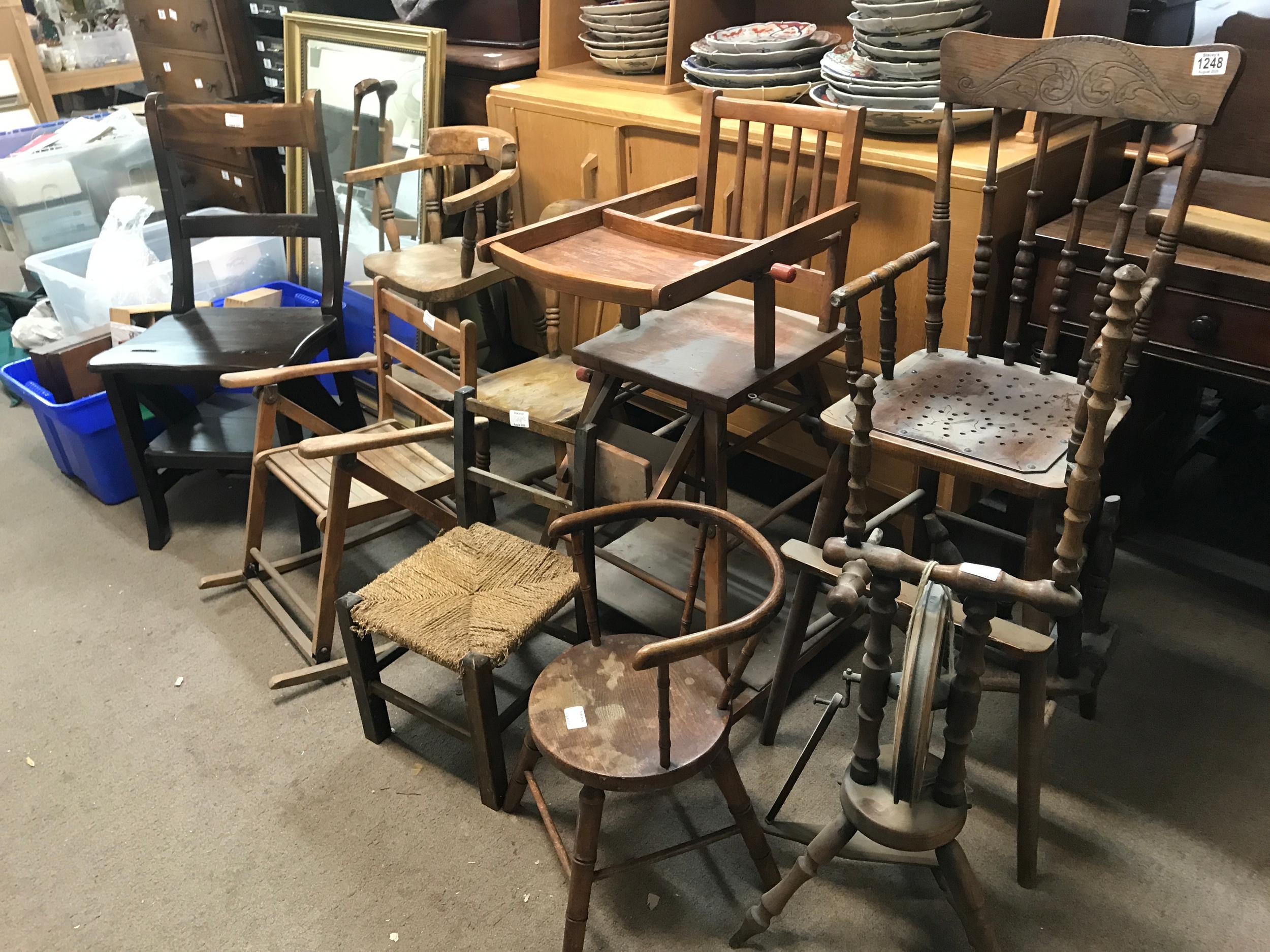 A collection of antique and vintage wooden children's chairs, dark wood metamorphic library chair, high chairs, miniature seating, and a traditional spinning wheel.