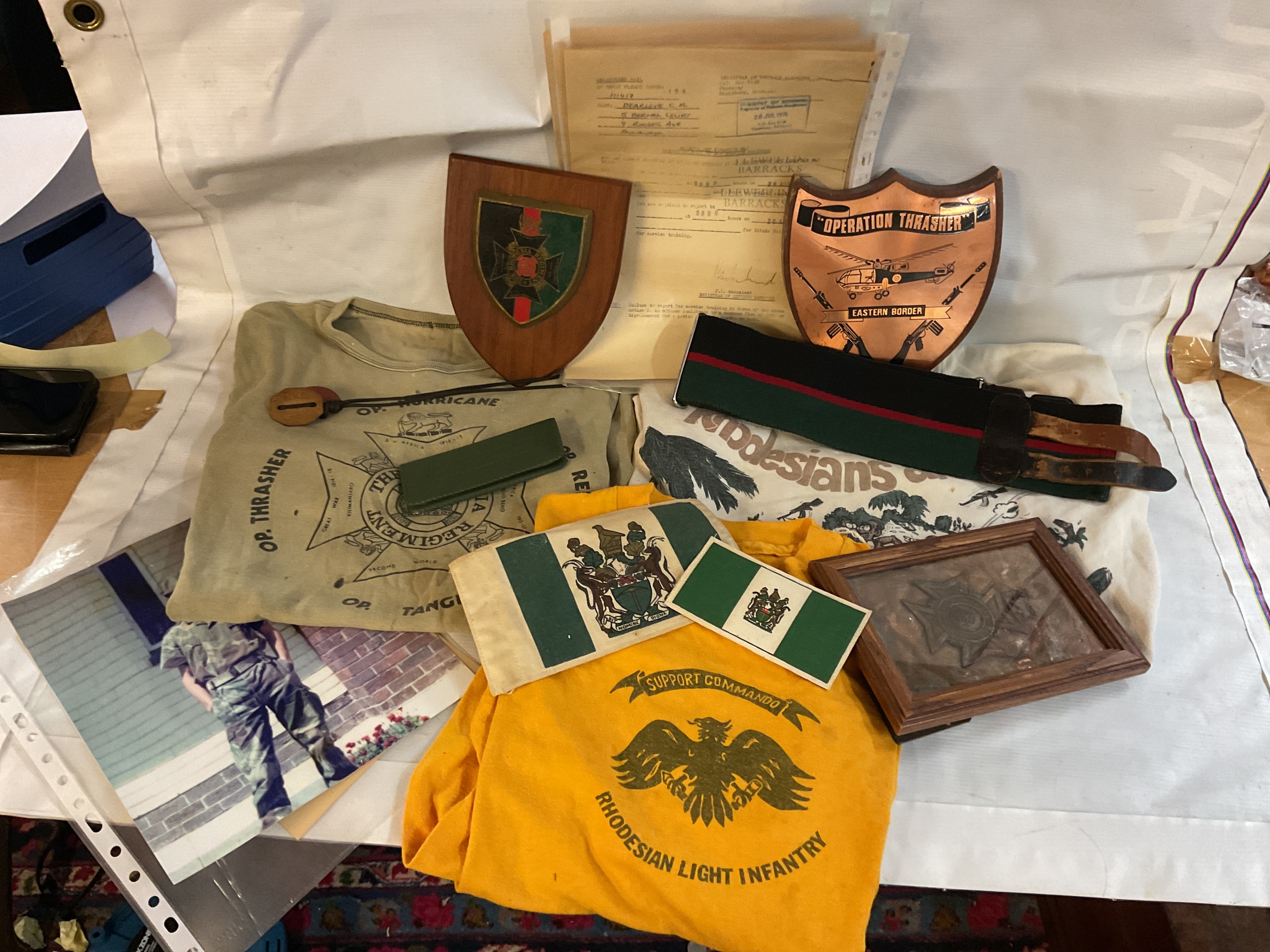 Rhodesian Army rare lot of Rifleman's kit to A Company, intake 154 3A Platoon, 1976-8, comprising field kit with full camo, shirts and hats, booney and kepi varieties along with stable belt, dog tags, paperwork for induction and rare unofficial platoon T-Shirts,  served in Operation Thrasher which covered the eastern border of Rhodesia facing Mozambique and experienced heavy infiltration by ZANLA insurgents. Important lot with history from the Twentieth century.three pairs of trousers and two jackets in DPM.