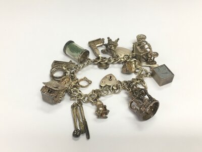 A silver charm bracelet including two charms containing bank notes, one shilling note and a £5.