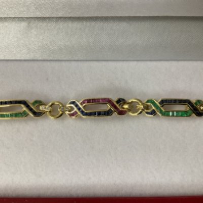 Exciting 18ct yellow gold ruby, emerald, sapphire and diamond &ldquo;figure of eight&rdquo; bracelet, boxed. Rubies 0.50ct approx. Sapphire 0.50ct approx. Emeralds 0.40ct approx. Diamonds 0.25ct. Postage category A.