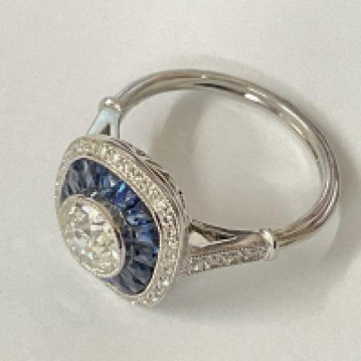 Stylish platinum dress ring set with a central old cut diamond surrounded by calibre cut sapphires, with eight cut accent diamonds framing and in the shoulders, featuring a filigree pattern. Centre diamond 0.85ct. Sapphires 0.65ct. Remaining diamonds 0.15ct. Ring size approx L. Postage category A.