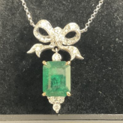 18ct white and yellow gold pendant set with a step cut emerald with RBC diamonds set below, and a diamond set large bow bale with integral 18ct white gold chain, boxed. Emerald 4.59ct. Diamonds 0.74ct. Postage category A.