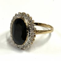 A 9ct gold ring set with a large blue central sapphire and surrounded by small cut diamonds. (A)