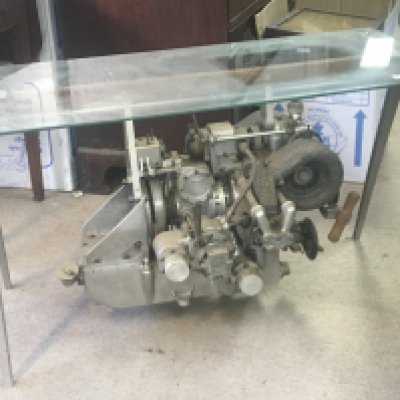 An unusual Steam punk type coffee occasional table the glass top above a Vintage car engine suspended on aluminium supports. 98x46cm