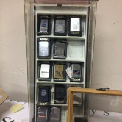 A display case containing Zippo lighters American Police theme and others and collection of conforming lighters in a box.