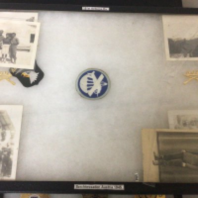 A framed display containing American II world war photos including some of personal from 101 Airborne division. A letter to the troops Allied Expeditionary Force American police badges and other cloth badges.