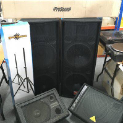 A collection of PA system equipment comprising a boxed Behringer Eurorack MX3242X 32 input mixing console, a pair of boxed Intimidation AKA 215 MKII speakers, two wedge monitors and stands.