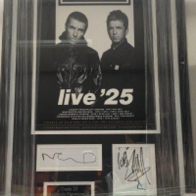 A framed and glazed Oasis '25 display signed by Liam and Noel, approx 72cm x 44cm.