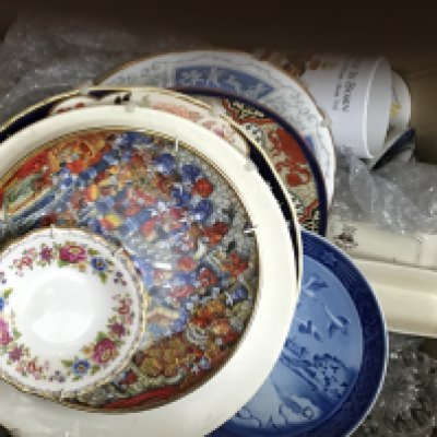 A box containing a large collection of commemorative ceramic mugs and decorative plates.