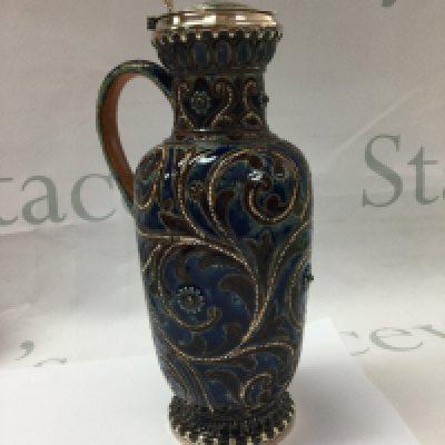 A Doulton Lambeth stoneware jug decorated with flower heads with silver plated lid 22 cm .