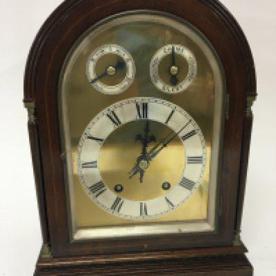 An Edwardian Mahogany mantel or table clock the arch case with pillar ornamentation with a brass dial and two subsidiary silver dials the brass movement striking on a double gong with pendulum. Height 36cm