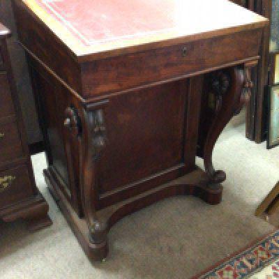 A William IV figured mahogany Davenport the hinged top enclosing a well fitted interior with satinwood drawers the scroll supports with raised floral roundels the side cupboard with a flight of four satinwood drawers.