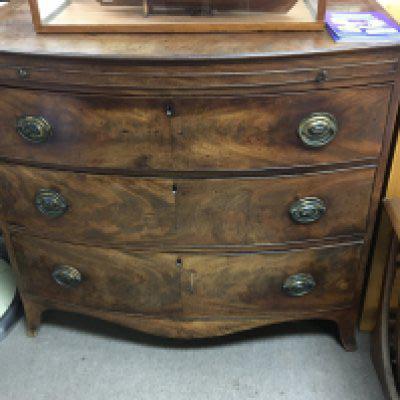 A late George III mahogany bow fronted chest of drawers fitted with a brushing slide above three drawers on swept bracket feet. 101cm long.