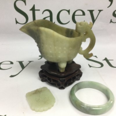 Three jade items comprising a carved jug, raised on a hardwood stand, a bangle etc. Shipping category D.