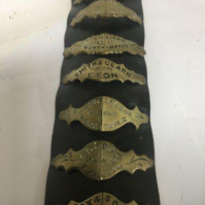 An antique leather strap mounted with brass horse harness nose bands each engraved with different harness makers and other horse brasses.