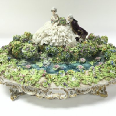 A large Dresden fine porcelain figurine. Repair to front right leg and damaged noted on dress and areas of foliage. 37cm wide 16cm tall