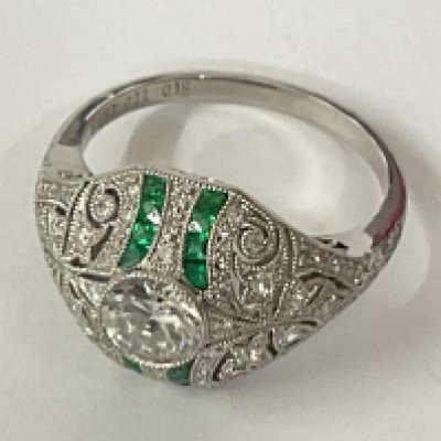 Platinum emerald and diamond dress ring with ornate, beaded setting. Centre diamond 0.57ct. Calibre cut emeralds 0.18ct. Accent diamonds 0.22ct.