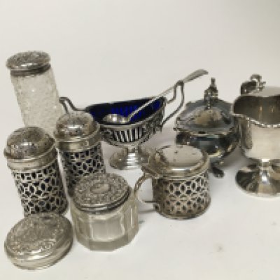 A collection of silver condiments a silver egg cup and glass tidy jars with silver lids.