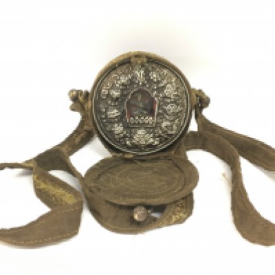 Tibetan travelling shrine figure of Buddha under glass behind embossed Tibetan silver front. This lot cannot be posted