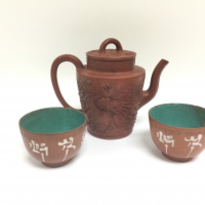 A terracotta teapot with applied decoration depicting a peacock and a pair of terracotta tea bowls (3). Shipping category D.