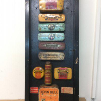 A mounted display of twelve vintage puncture repair kits. Shipping category C.