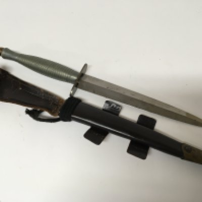 A Fairbrain Sykes Commando fighting knife with an aluminium coloured cast handle in a leather scabbard.