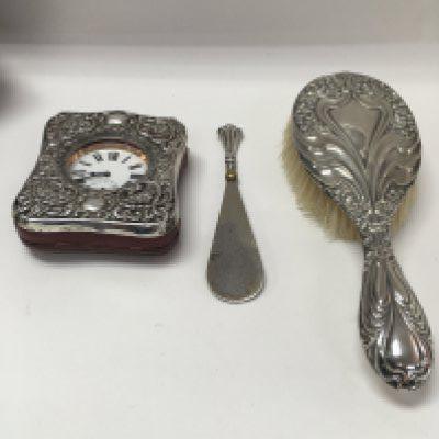 A collection of silver items including a hair brush, a shoe horn and a clock case.