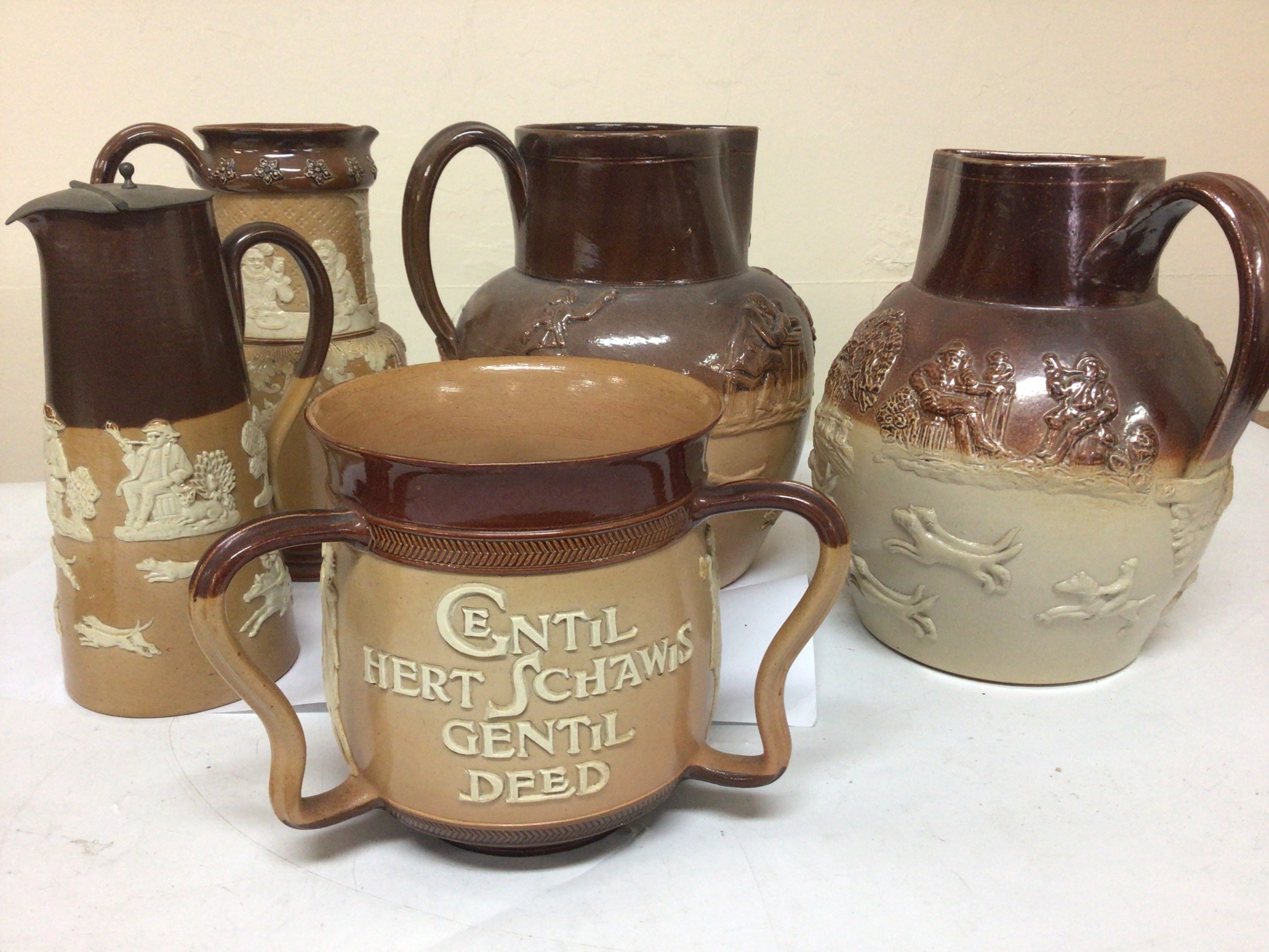A Lambeth Doulton stoneware loving cup with the Nobel inscription'A Gentle Heart shows a Gentle deed" slight chip to the rim and other Lambeth and Royal Doulton stoneware jugs (5) 