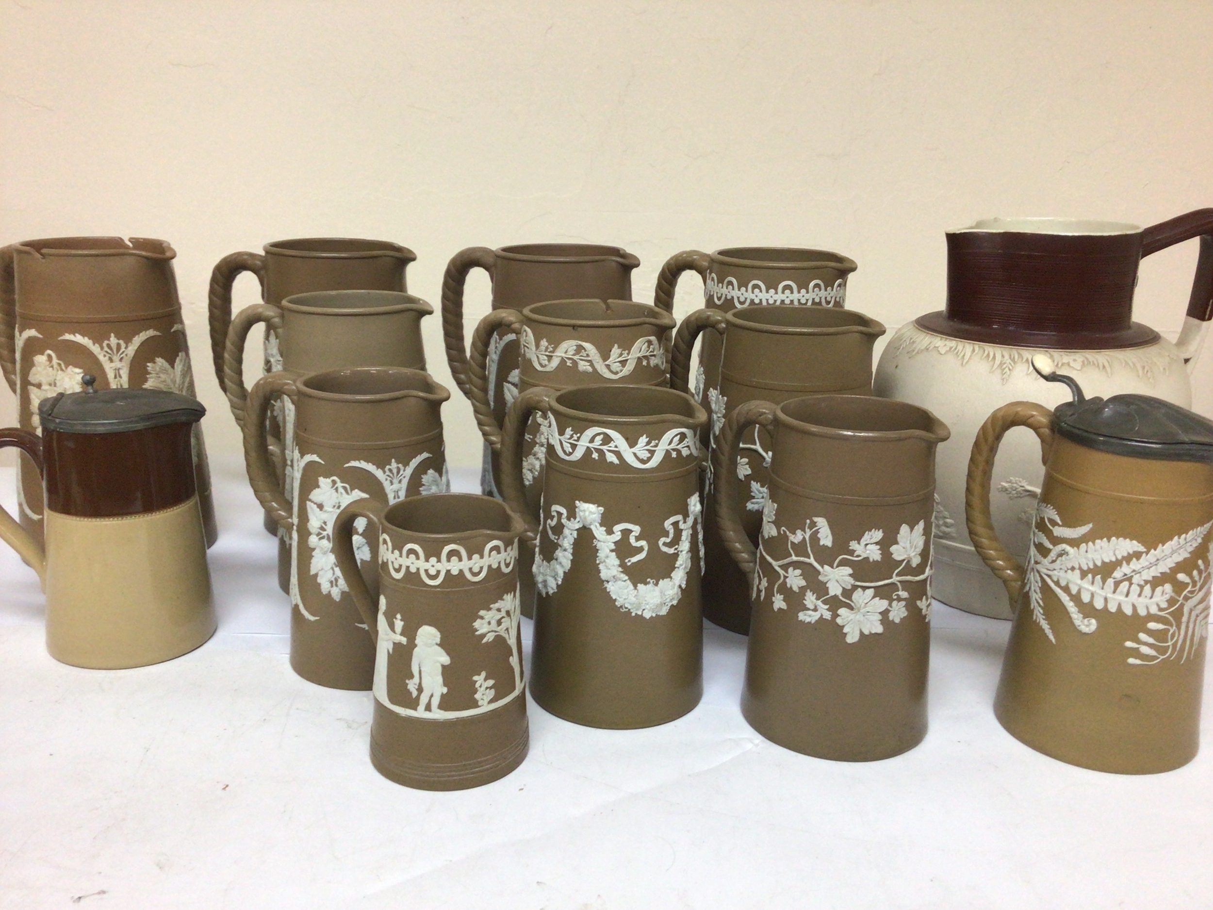  A collection of Victorian brown and white jugs decorated with white sprigging with garlands of flowers other foliage and neo-classical figures. possibly Dubson Bro and one other moulded Ceramic Victorian Pitcher. No obvious damage except missing pewter lids maximum Hight 20cm 