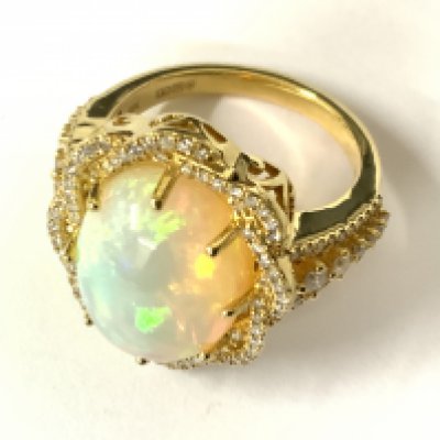 9ct yellow gold ring set with an oval cabochon opal within a twist style diamond surrounded by RBC, with further diamonds to the shoulders. Opal 6.85ct. RBC diamonds 0.59ct. Approx ring size O/P. Postage category A