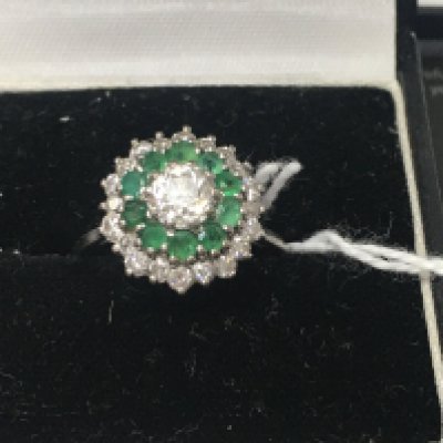 A 18 ct white gold ring inset with central diamond surrounded by emeralds and further diamonds. Size J