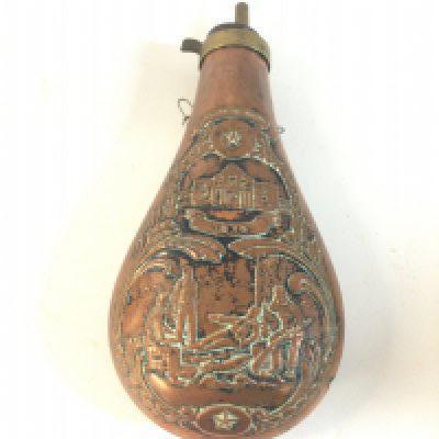 A brass and copper powder flask with an image of soldiers and the date 1836.