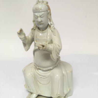 A Chinese Blanc de Chine figure of the god of war Guandi the figure possible 18th century or earlier. The seated figure holding a scroll height 29cm. Has damage and restoration and a large firing crack to the reverse the glaze crackled.