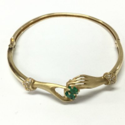 A 14ct gold crossed hands bangle inset with two Colombian green emeralds and pave set diamonds. 9.80g