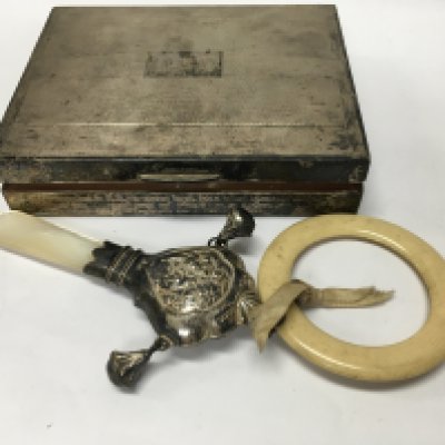 A small silver cigarette box together with a childs rattle.