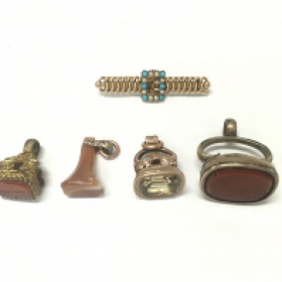 Four antique seals of various designs and a yellow metal brooch.