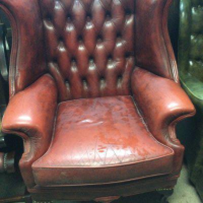 A red leather wing armchair with button back on cabriole legs .