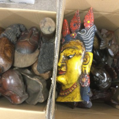 Two boxes of carved wooden items comprising tribal masks and ornaments. Shipping category D.