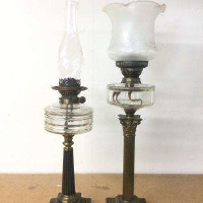 Tw oil lamps with clear glass reservoirs, one raised on a Corinthian column. Shipping category D.