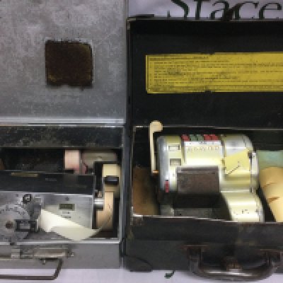 Two vintage bus conductor's ticket machines, one manufactured by Almex plus one other, unused rolls of tickets and both housed in original carry cases (2). Shipping category D.
