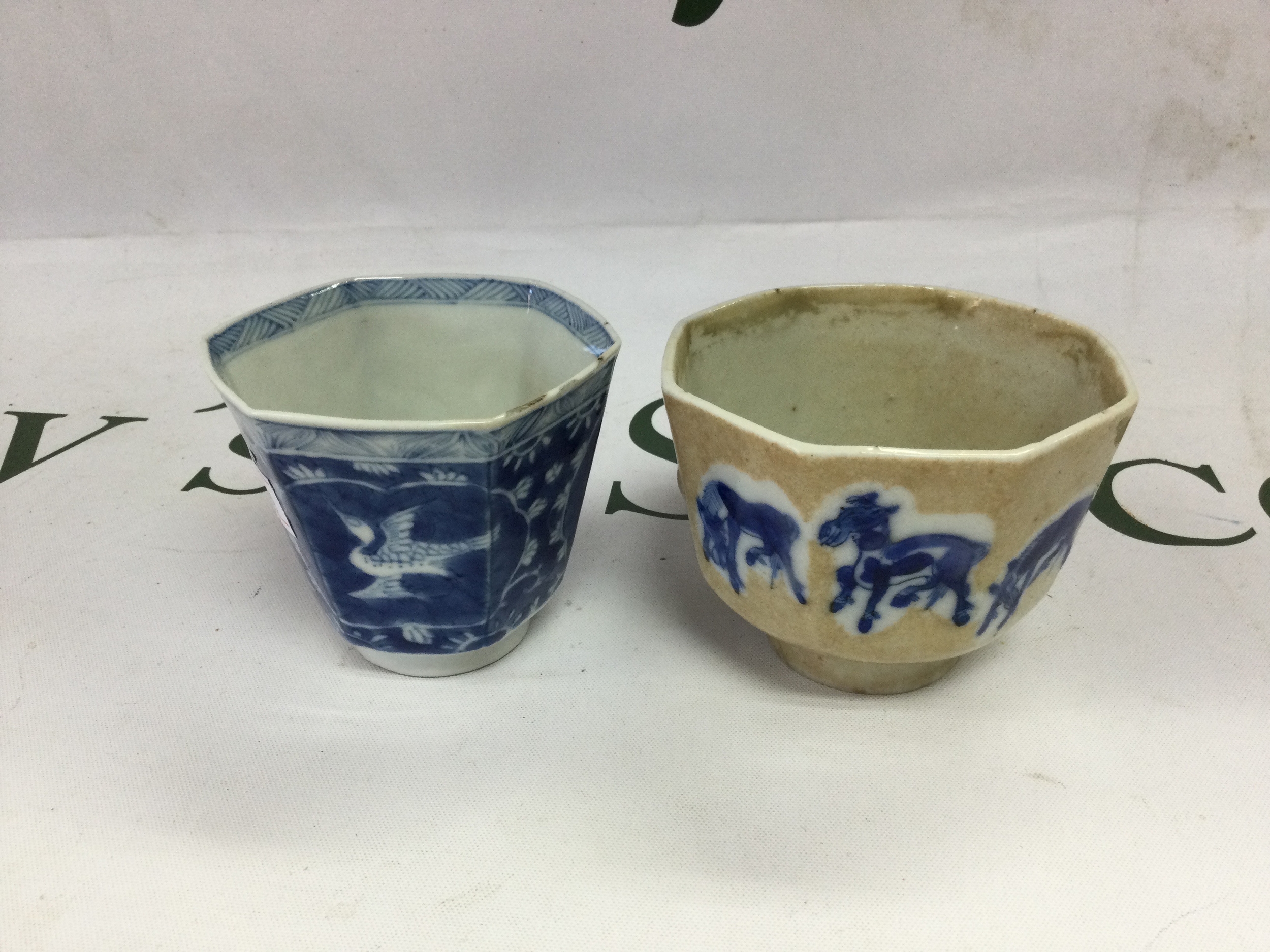 Two 18th C Chinese cups Kang Xi period mark to damaged cup of earlier dynasty, Hexagonal cup bearing Kang Xi character inside concentric circles and decorated with Ho Ho birds in cartouches, minor flitting to the rim, the octagonal example depicting eight different drawn horses in blue within a tea glaze, damage to the foot, bearing a four character mark to the base.